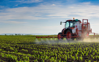 tractor spraying atrazine pesticide onto a field of corn