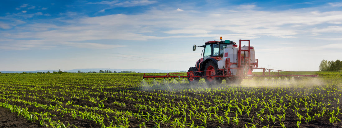 tractor spraying atrazine pesticide onto a field of corn