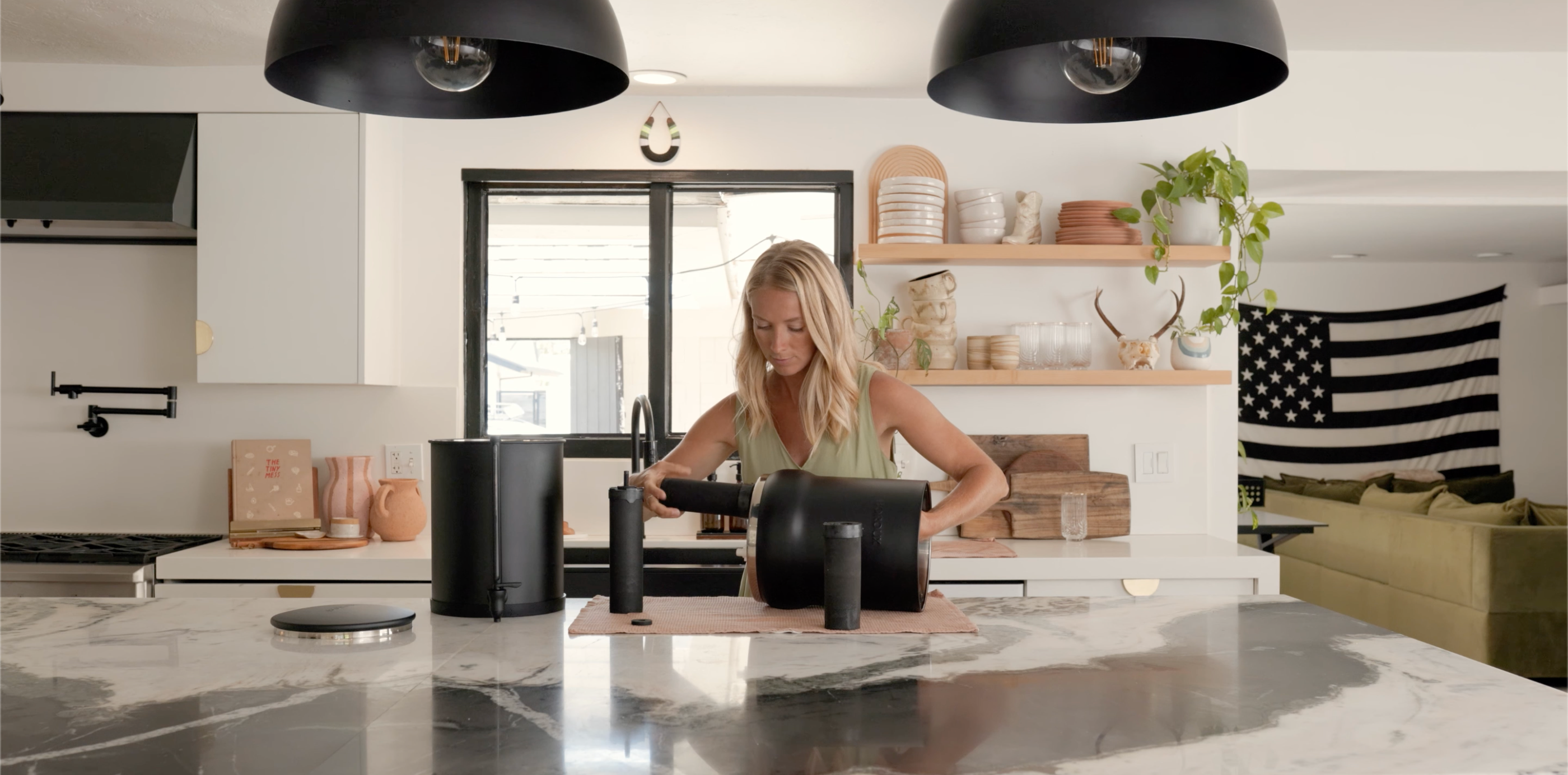 Woman using a tablet in a modern kitchen with black pendant lights and an American flag decoration.