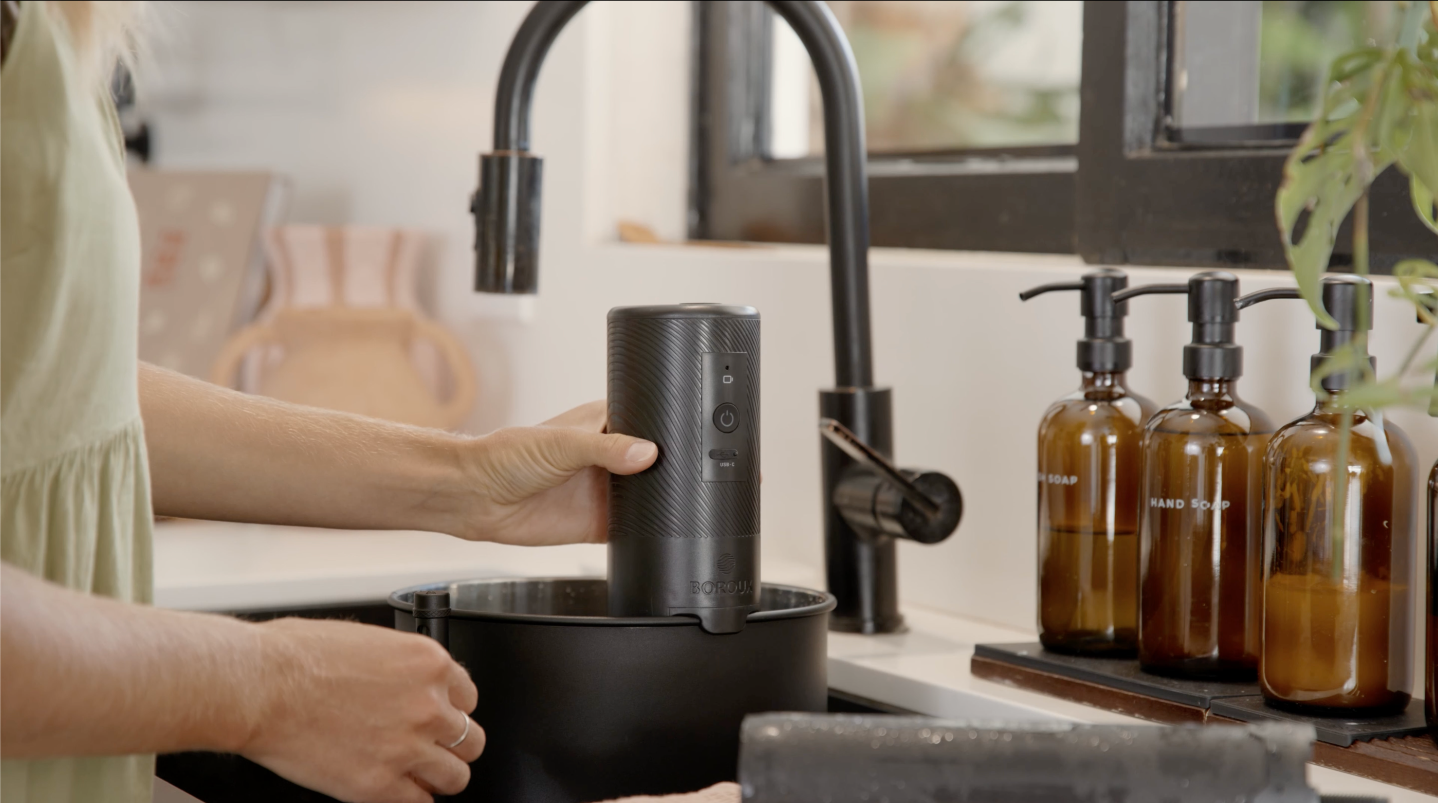 Person washing a black mug in a kitchen sink with brown bottles on the counter.