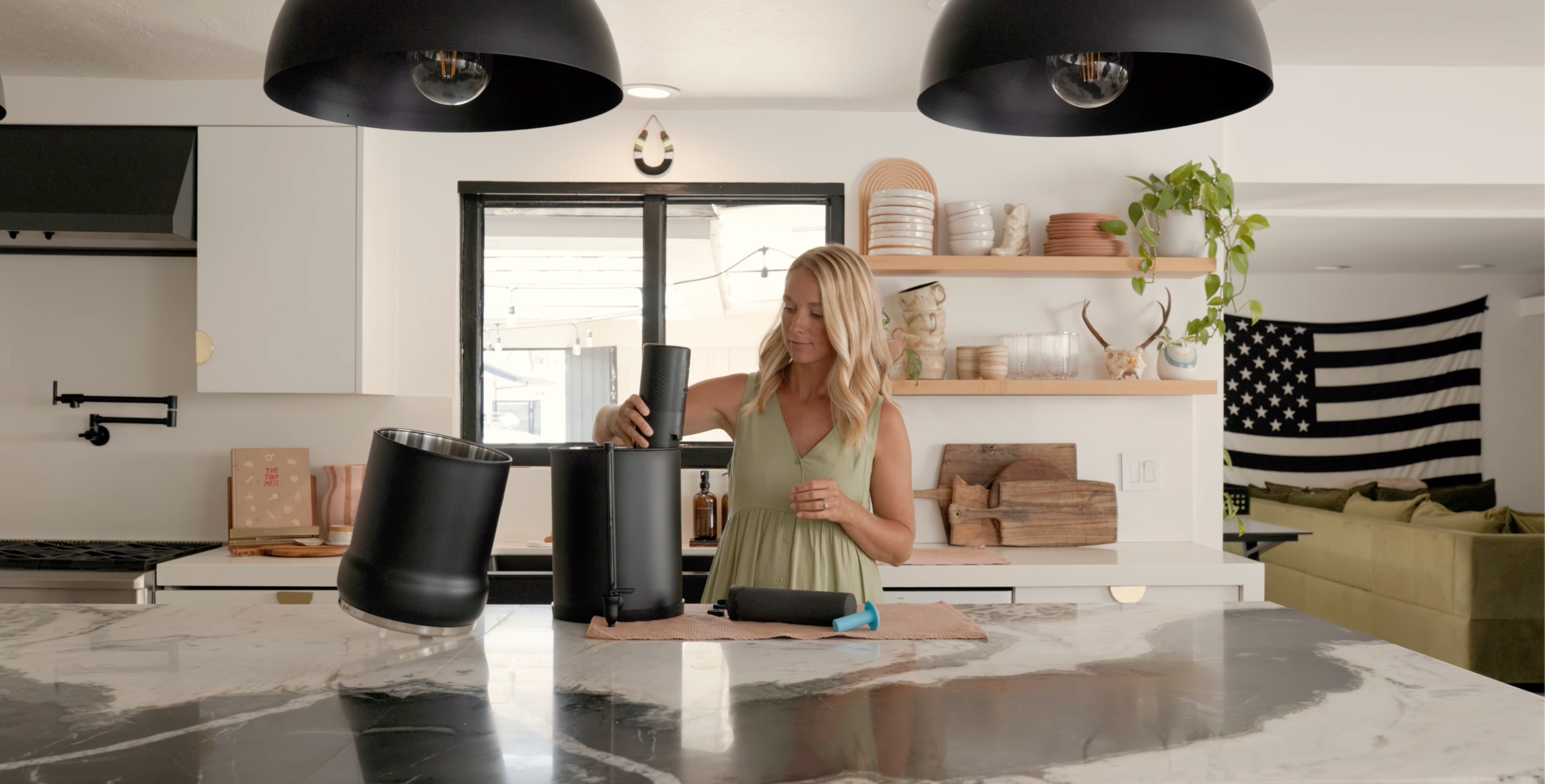 Woman standing in a modern kitchen with black pendant lights and a white countertop.