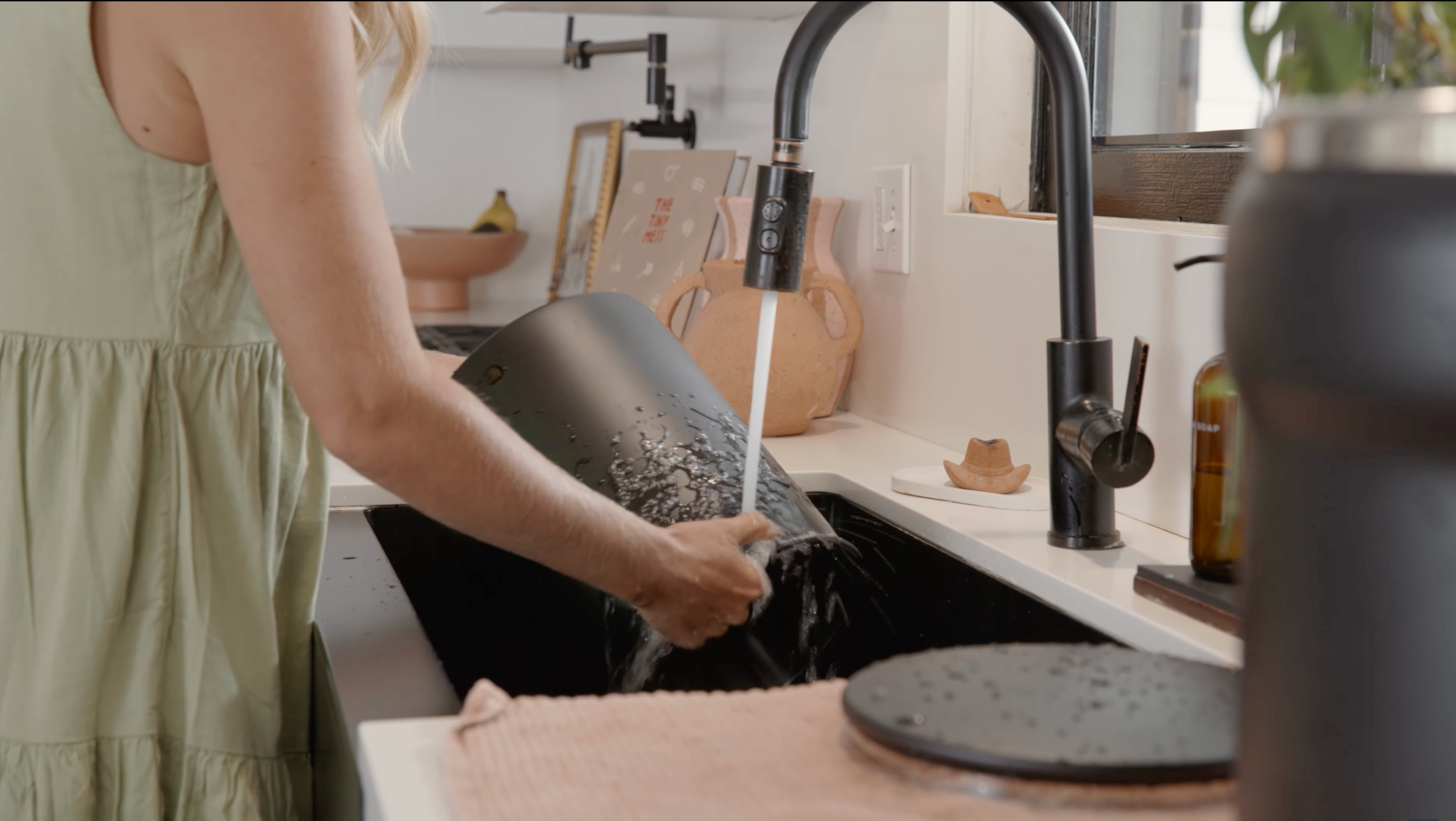 Person washing dishes in a kitchen sink with a black faucet.